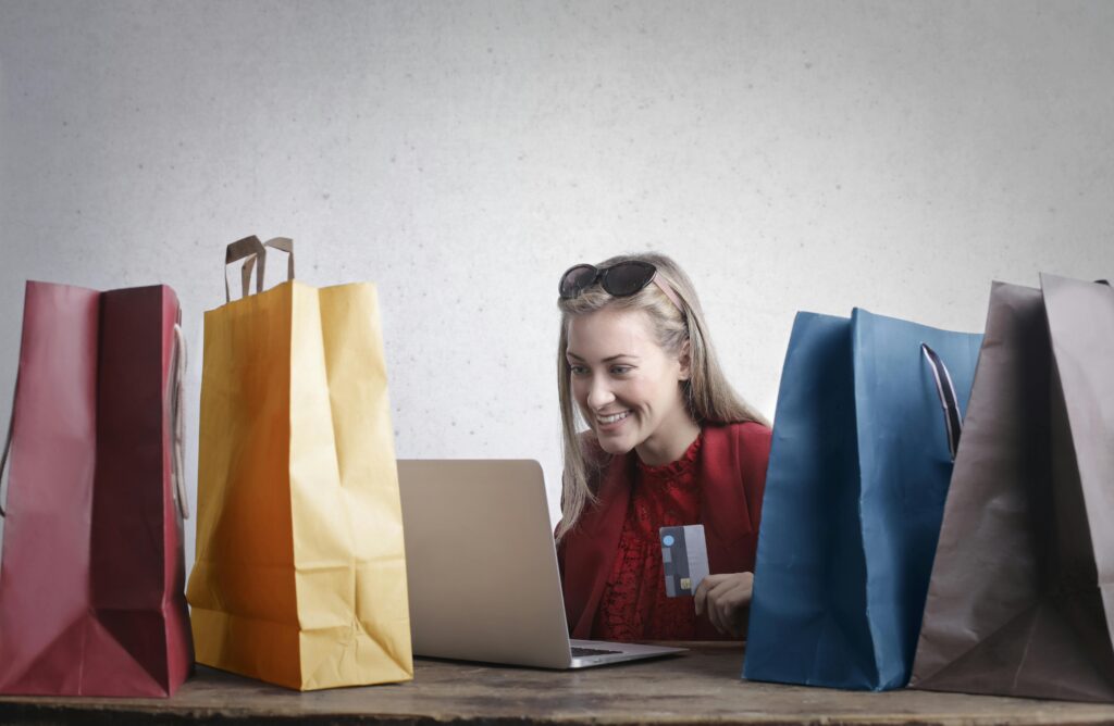 pexels-photo-3769747-3769747 A joyful woman shopping online using a laptop with colorful shopping bags surrounding her.